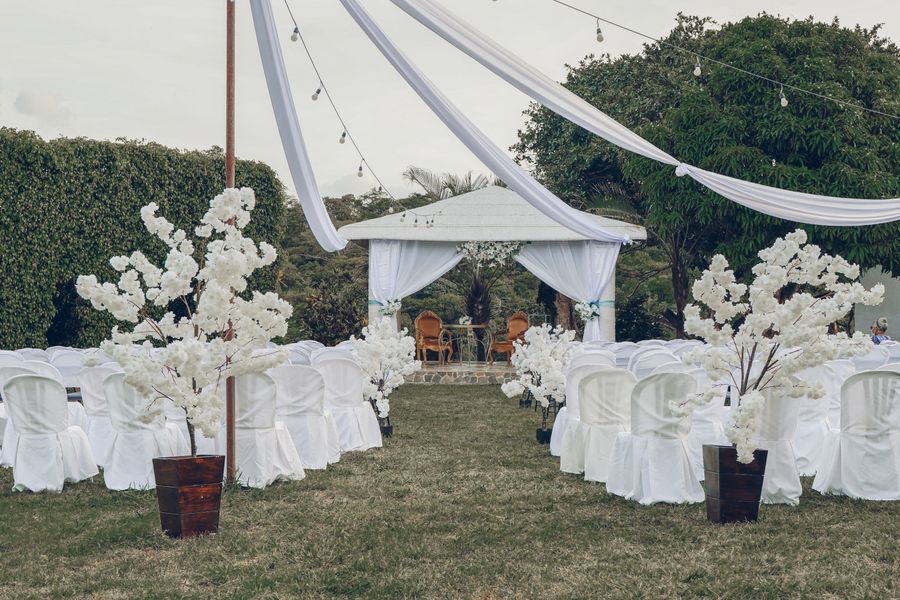 Cérémonie de jardin : allée de chaises blanches et arche fleurie devant le pavillon
