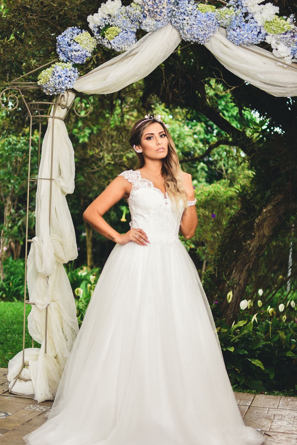 Mariée posant sous une arche fleurie d'hortensias dans le jardin