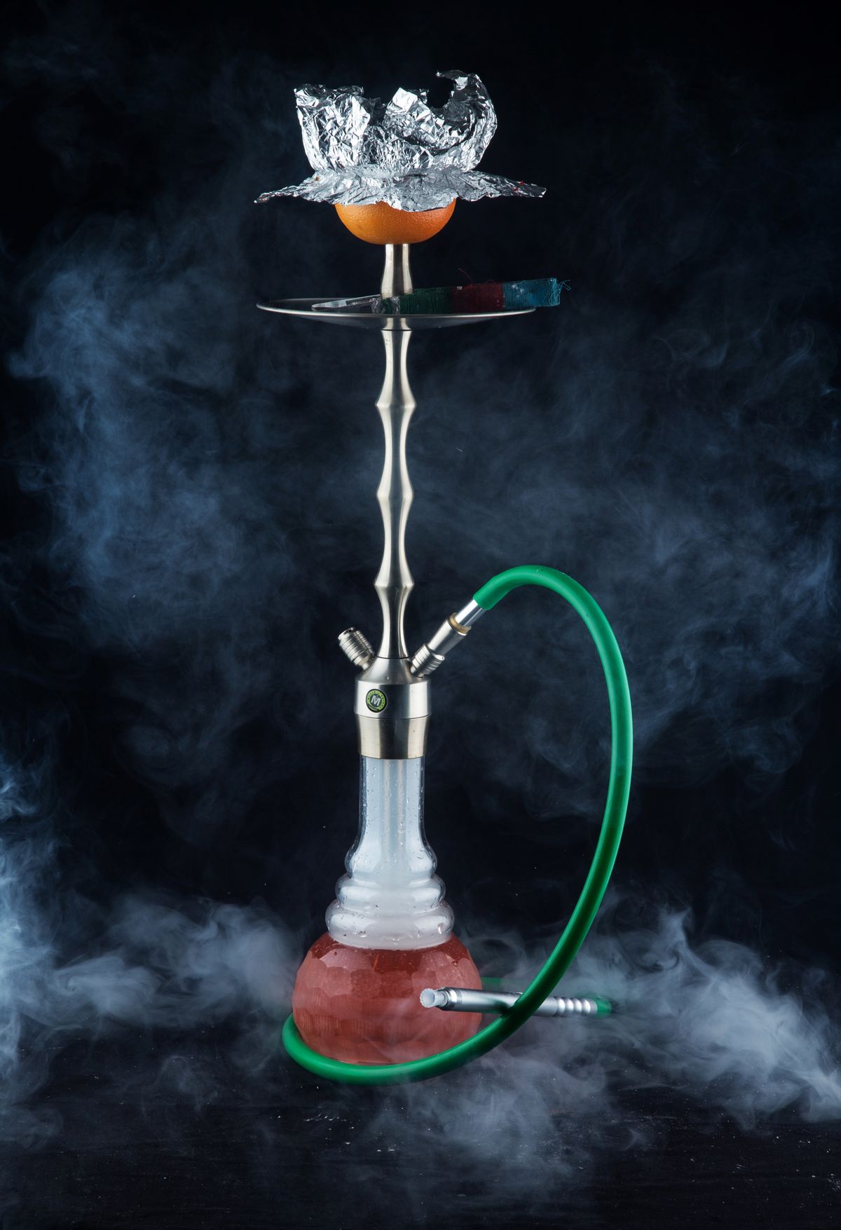 Narguilé (chicha) posé dans une lumière tamisée, volutes de fumée sur fond sombre