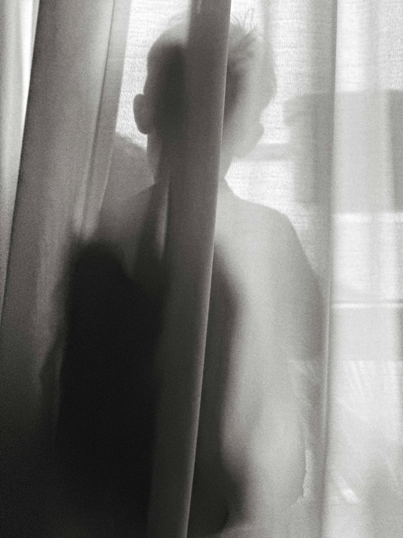 Silhouette à contre-jour devant une fenêtre voilée